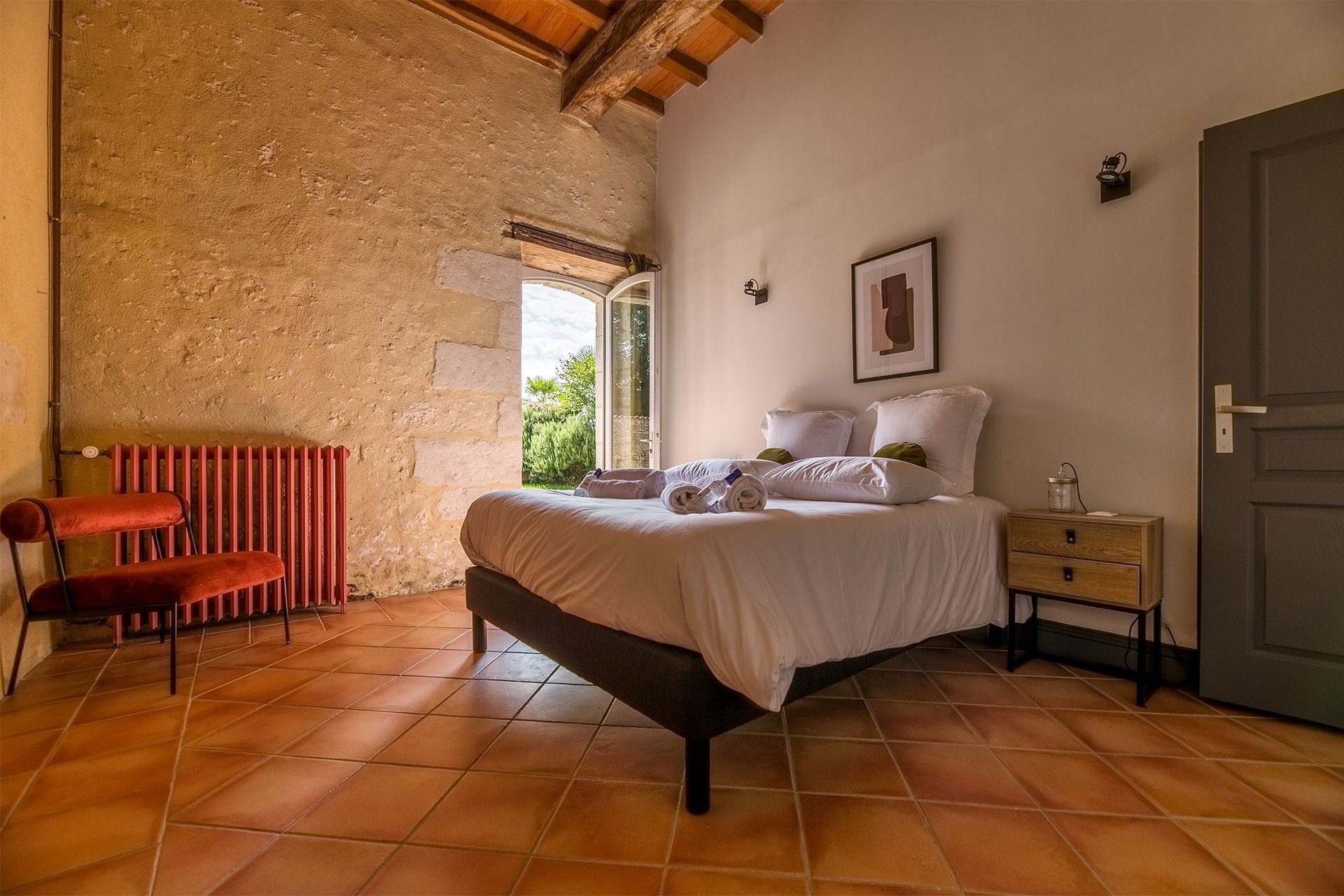 A bright guest bedroom with terracotta floor tiles and beamed ceiling